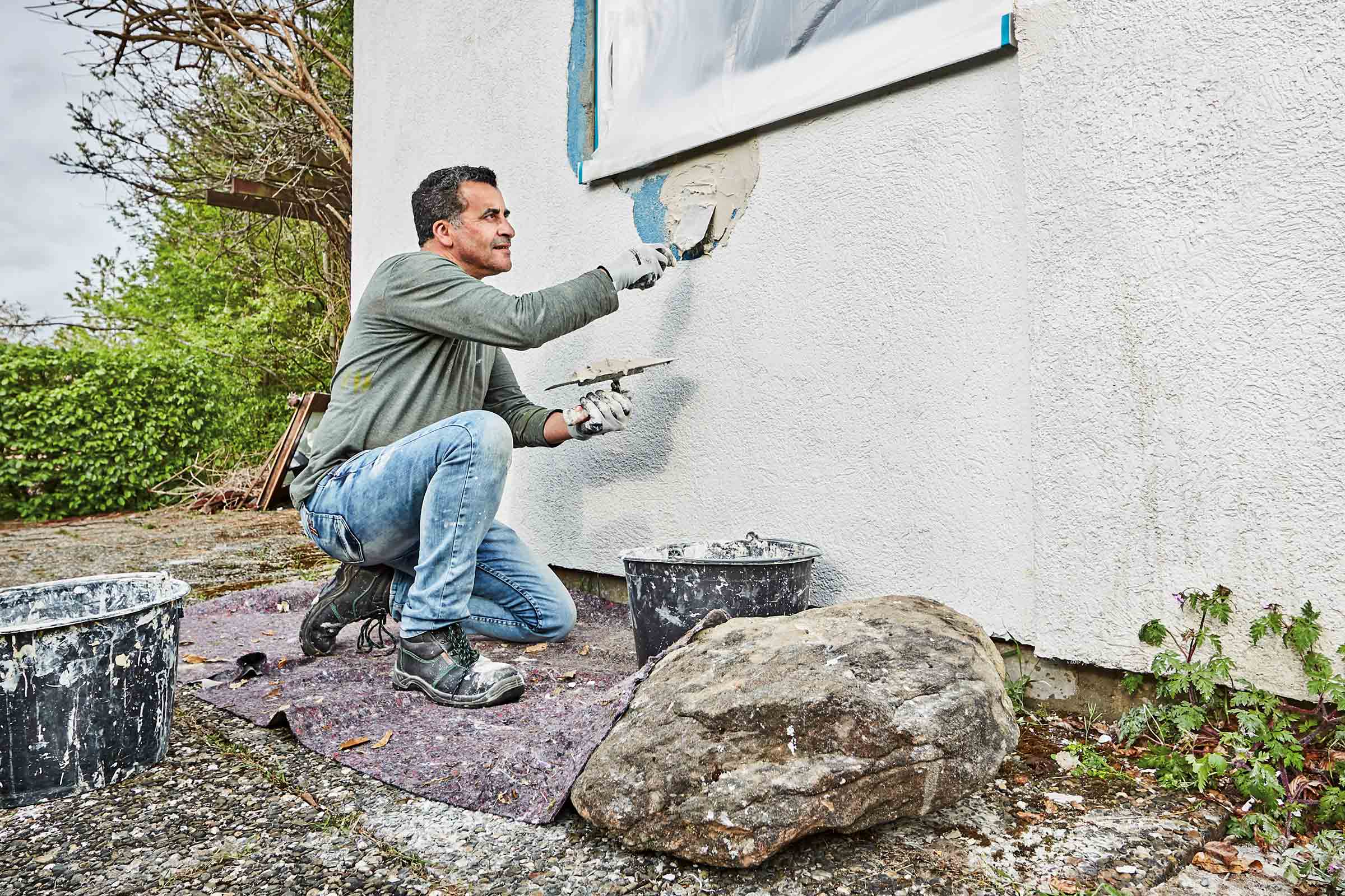 Handwerker bei der Fassadenrenovierung mit Spachtel und Putz.
