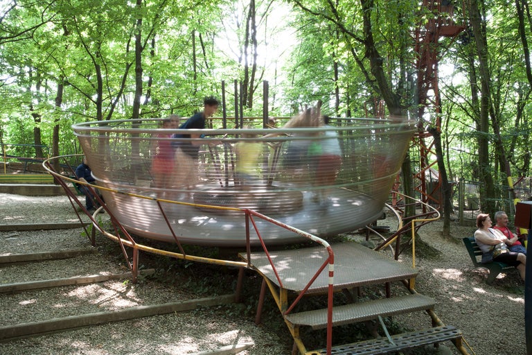 Szene im Freien mit einem sich drehenden Karussell und Personen in einem Park.