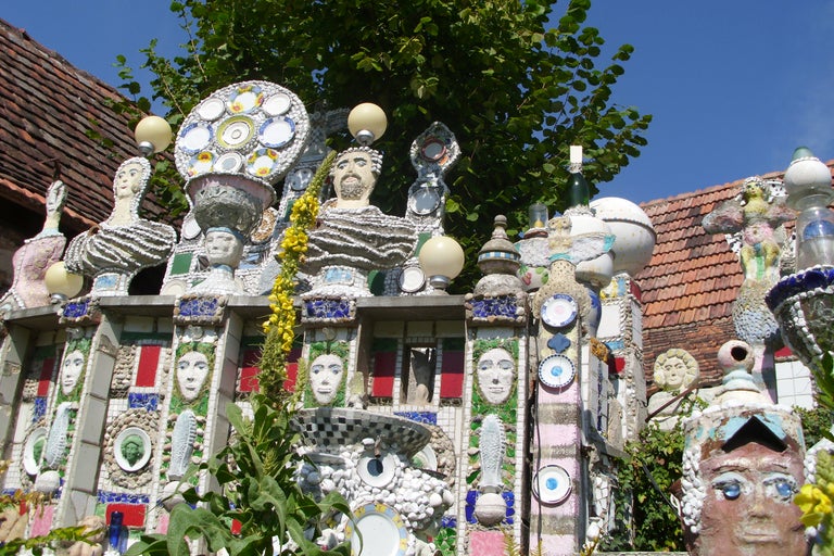 Detailansicht eines kreativen Gartenzauns mit Mosaiken, Keramik und Skulpturen.