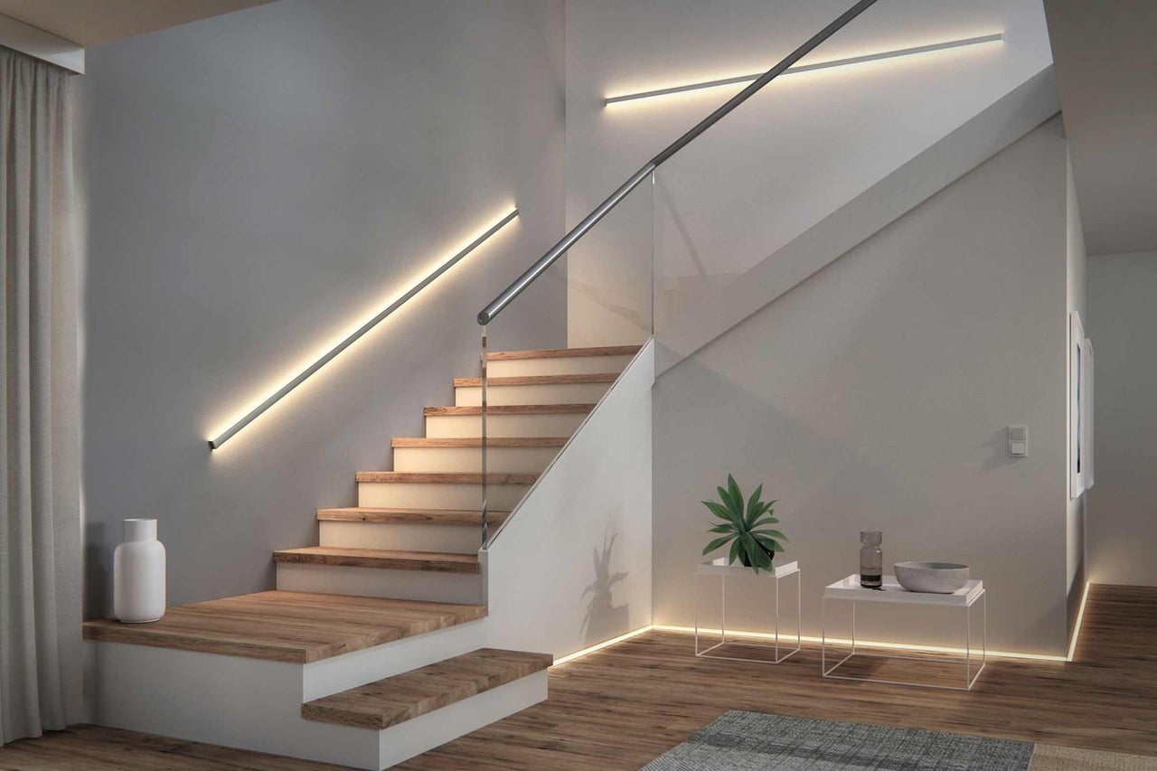 Treppenhaus mit Holzstufen, Glasgeländer und linearen Wandleuchten