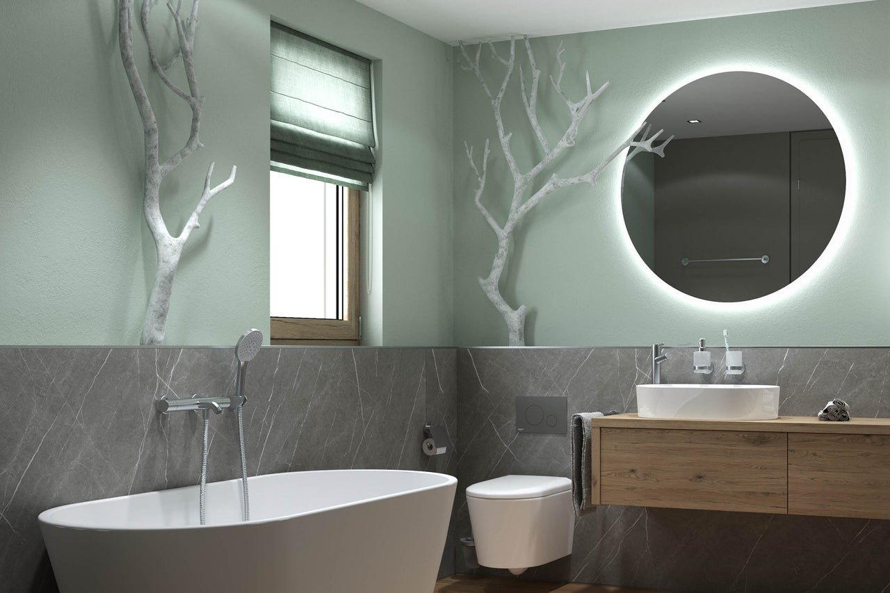 Modernes Badezimmer mit freistehender Badewanne, Wand-Toilette und Holz-Waschtisch. Ein rundum beleuchteter Spiegel und dekorative weiße Äste.