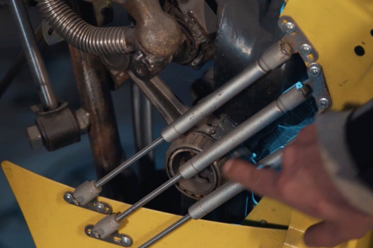 Detailansicht einer gelben Apparatur mit Metallstreben und einem Lager, das von einer Hand berührt wird.