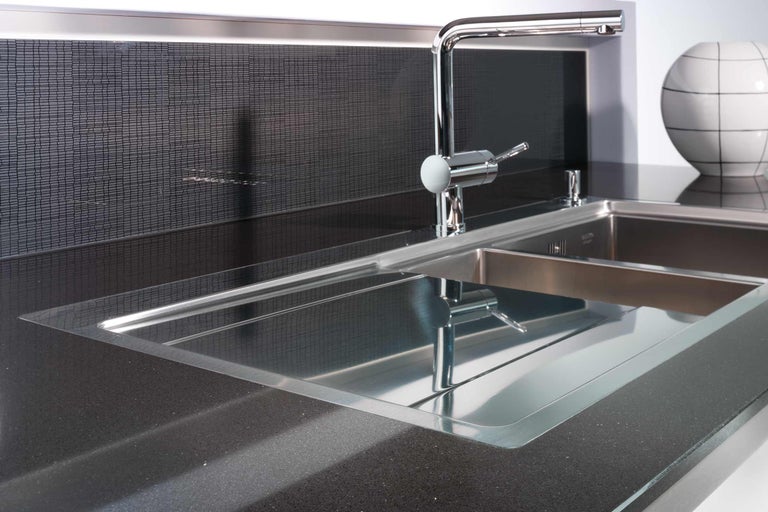 Spültisch aus Edelstahl mit Armatur auf dunkler Arbeitsplatte