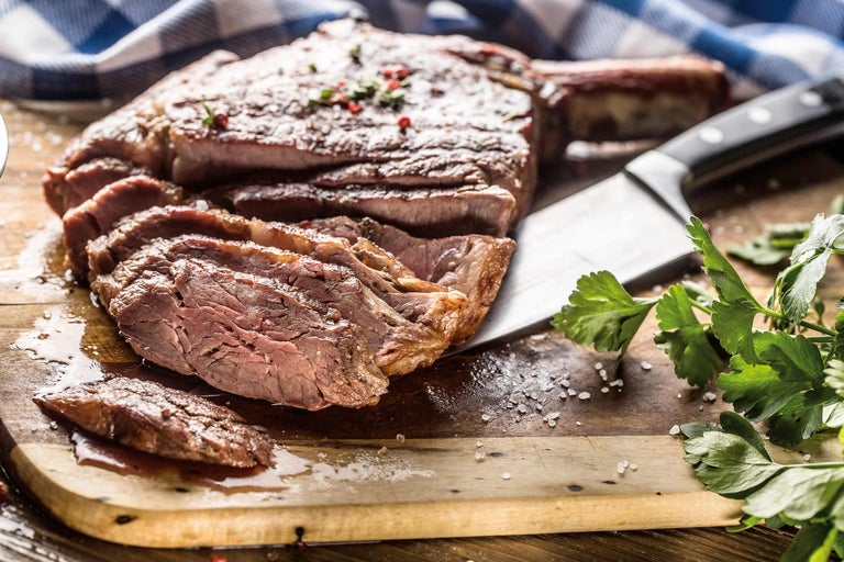 Tomahawk Steak, tranchiert, auf Holzbrett mit Messer und Petersilie