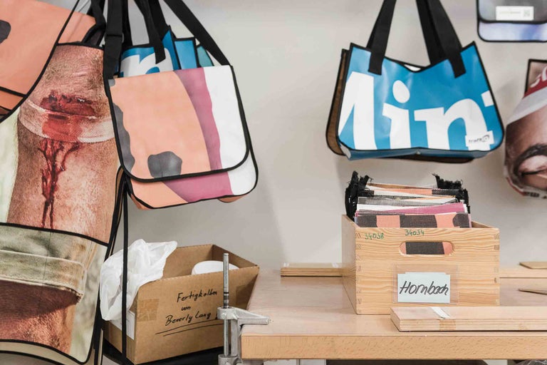 Mehrere Taschen mit unterschiedlichen Motiven hängen an einer Wand über einem Tisch.