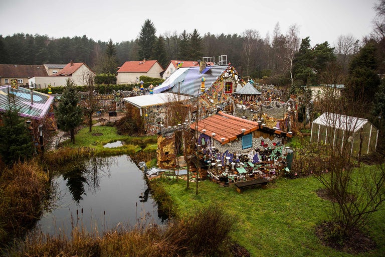 Ansicht eines Gartens mit einem Teich und einem Haus, das mit Mosaiken und Dekorationen verziert ist.