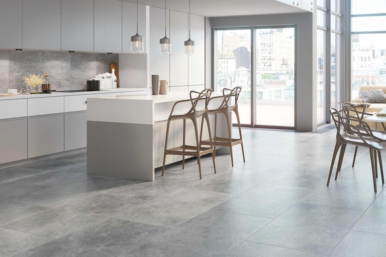 Helle Küche mit grauem Bodenfliesenbelag und Kücheninsel mit Barhockern.