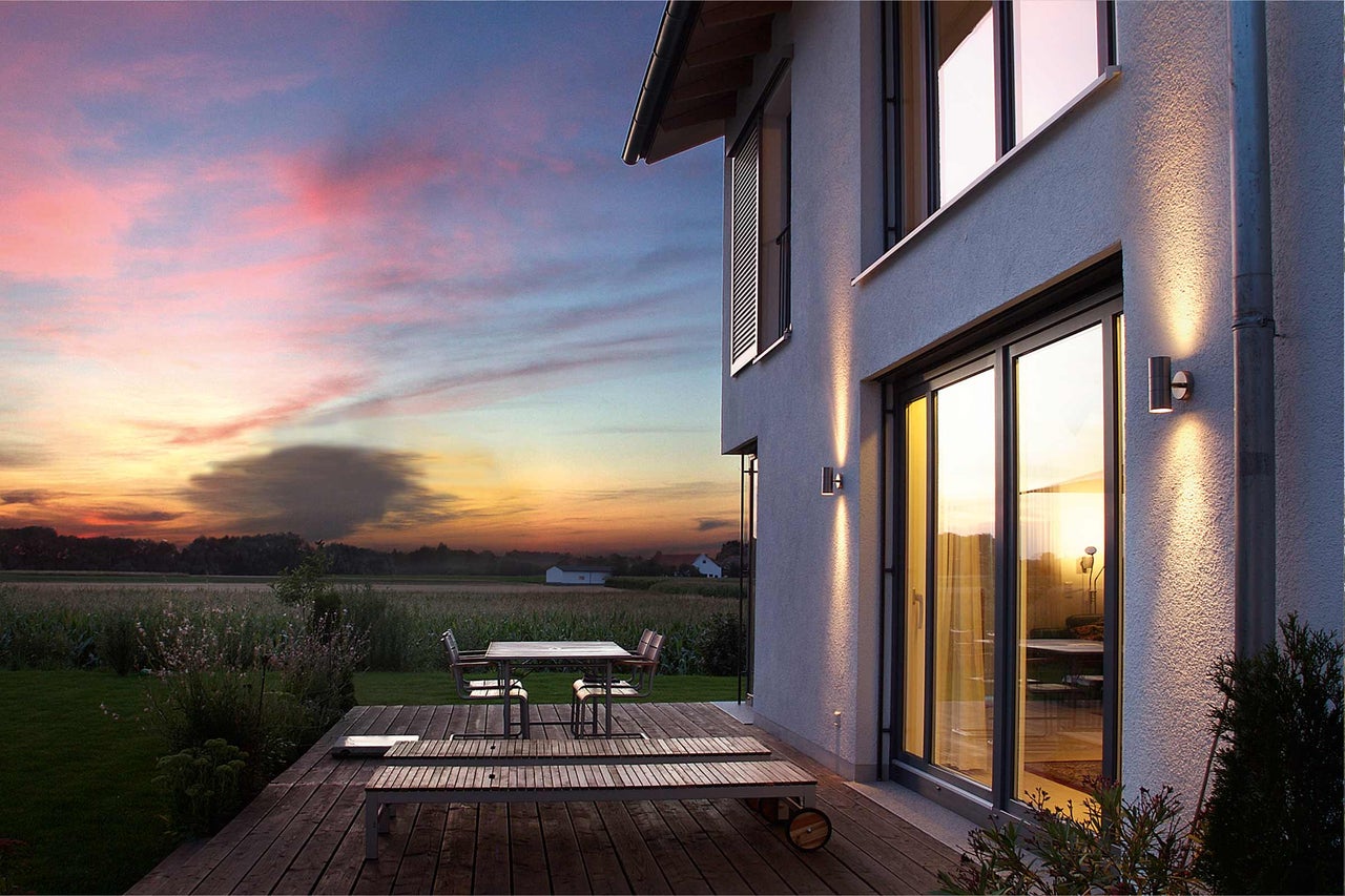 Außenansicht eines modernen Hauses mit Terrasse und Gartenmöbeln bei Sonnenuntergang