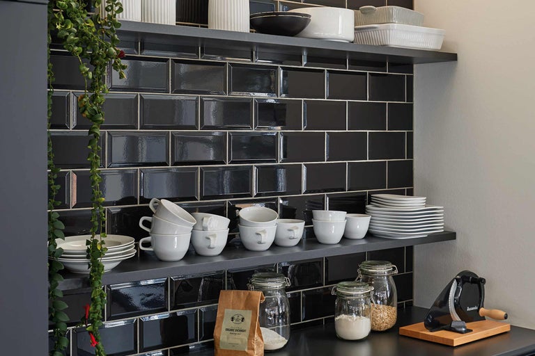 Regale mit Geschirr und schwarze Kacheln in der Küche