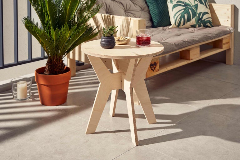 Runder Beistelltisch aus hellem Holz auf einem Balkon mit Getränk und Dekoration