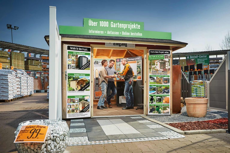 Außenansicht eines Informationsstandes für Gartenprojekte mit zwei Kunden und einem Verkäufer