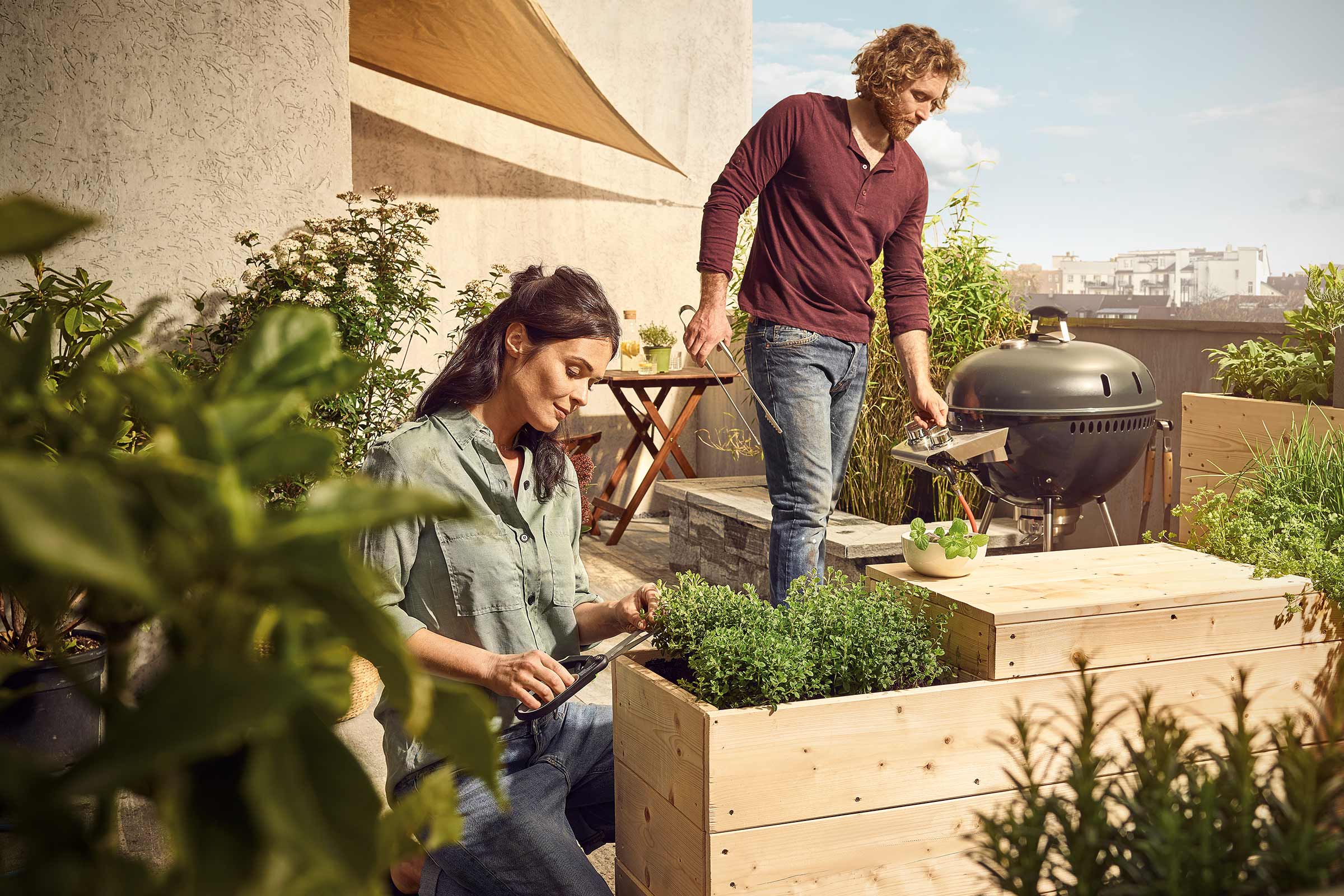 Personen gärtnern und grillen auf einer Dachterrasse mit Hochbeeten und Grill