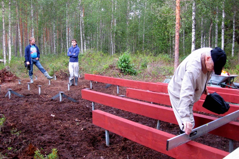 Drei Personen bauen ein Fundament aus Holz und Metallpfosten im Wald.