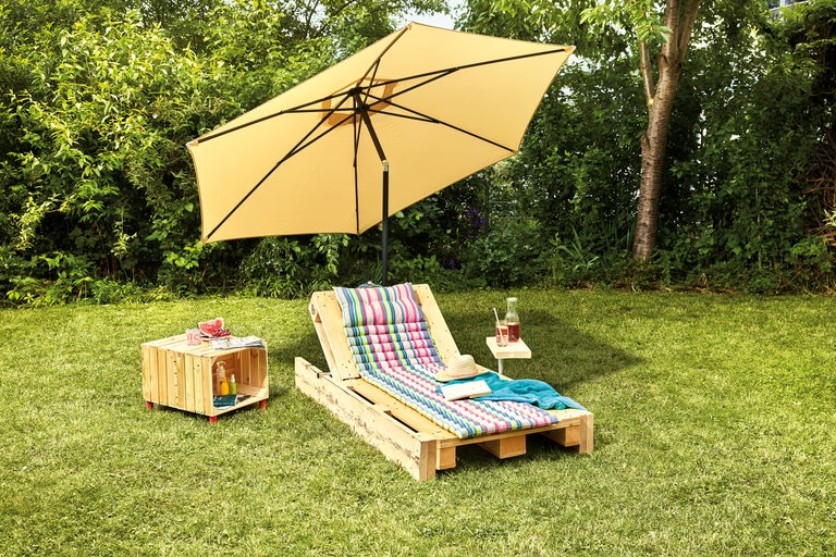 Szene im Garten mit Sonnenschirm, Liegestuhl aus Holzpaletten und Beistelltisch