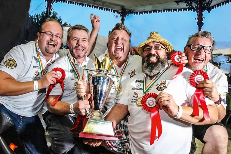 Fünf Männer feiern mit einer Trophäe und Auszeichnungen für einen Grillwettbewerb.