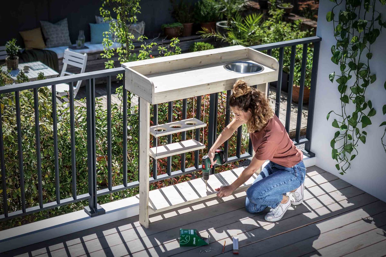 Frau montiert einen Gartentisch mit Spüle auf einem Balkon.