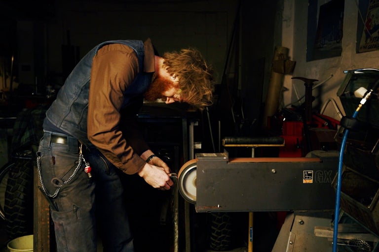 Ein Mann arbeitet mit einer Bandschleifmaschine in einer Werkstatt.