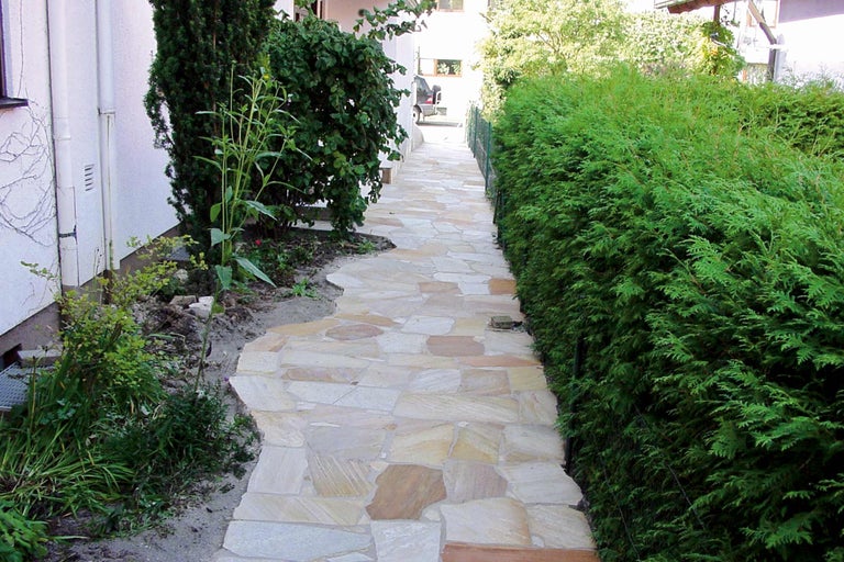 Gartenweg aus Natursteinplatten mit angrenzenden Grünpflanzen