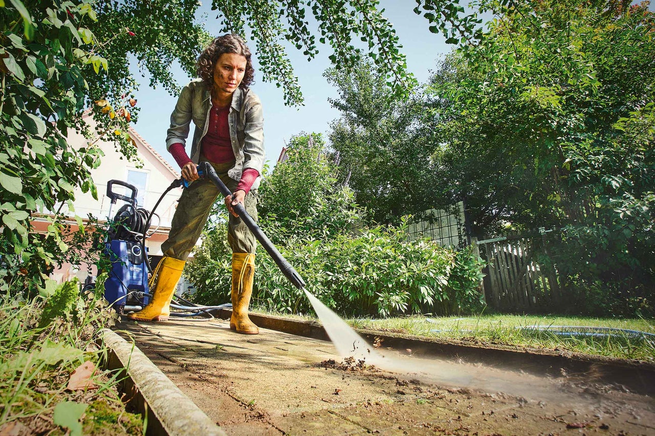 Frau reinigt Gehweg mit Hochdruckreiniger im Garten.