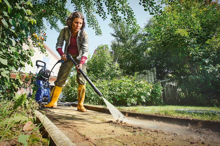 Frau reinigt Gehweg mit Hochdruckreiniger im Garten.