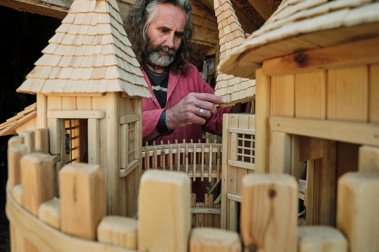 Mann baut Holzspielhaus mit Schindeldach