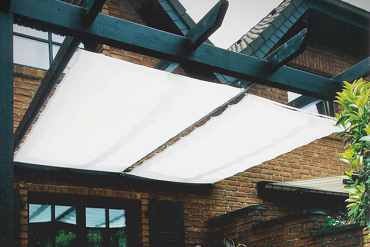 Pergola mit weißem Sonnensegel vor einem Backsteingebäude