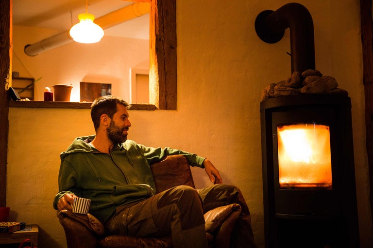 Mann sitzt in einem Sessel neben einem Kaminofen