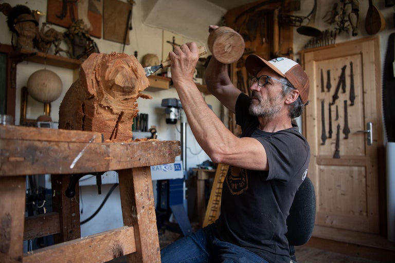 Ein Holzschnitzer bei der Arbeit an einer Holzskulptur mit Hammer und Stechbeitel in einer Werkstatt.