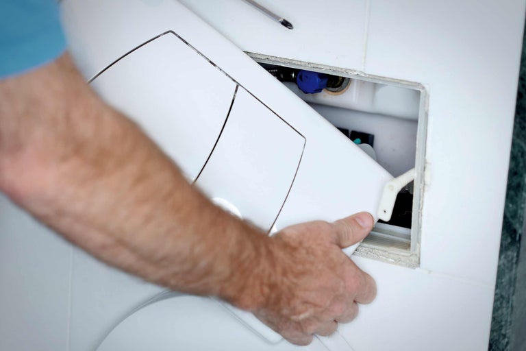 Eine Person montiert einen Toilettenspülkasten an einer Badezimmerwand.