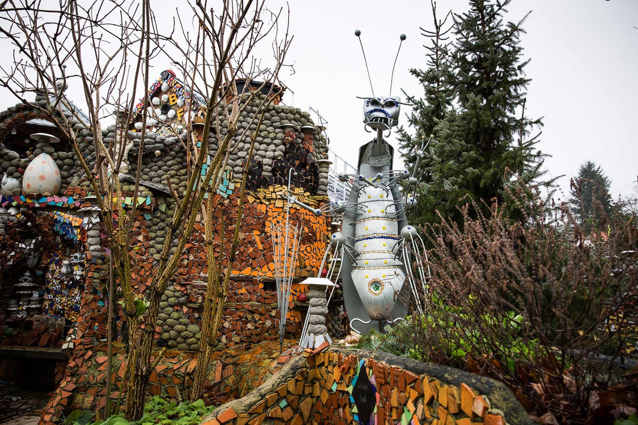 Garten mit einer Skulptur einer Figur und einem Haus mit Mosaikverzierungen.