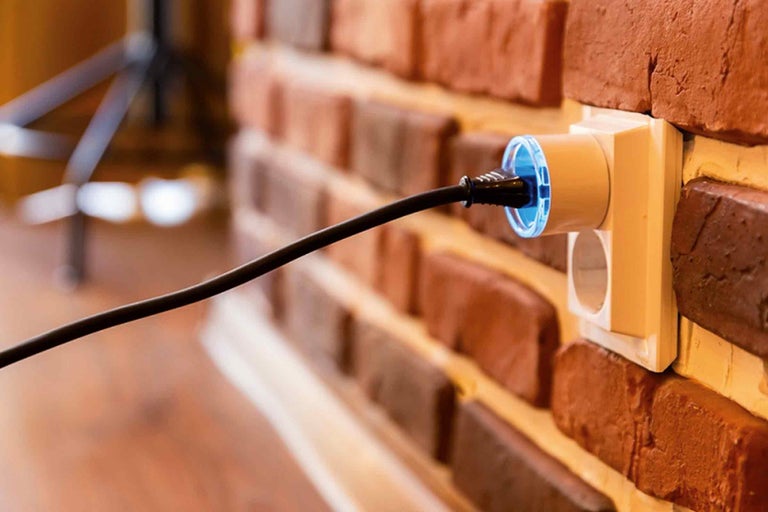 Steckdose mit eingestecktem Stecker an einer Ziegelwand