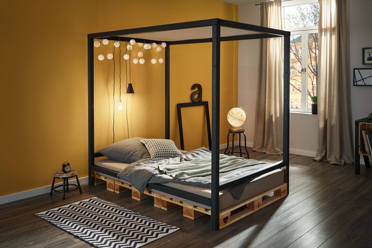 Schlafzimmer mit Himmelbett, Palettenbettgestell und dekorativer Beleuchtung