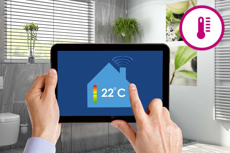 Person bedient ein Tablet im Badezimmer zur Temperaturregelung. Das Thermometer Symbol ist sichtbar.