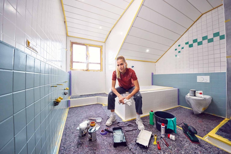 Ein Mann installiert ein Waschbecken in einem Badezimmer mit Fliesen, Badewanne und Werkzeugen.