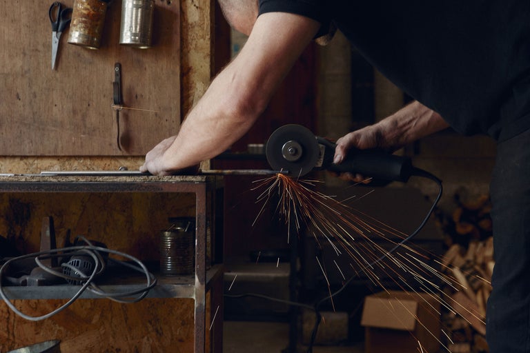 Ein Mann schneidet Metall mit einem Winkelschleifer, wobei Funken sprühen.