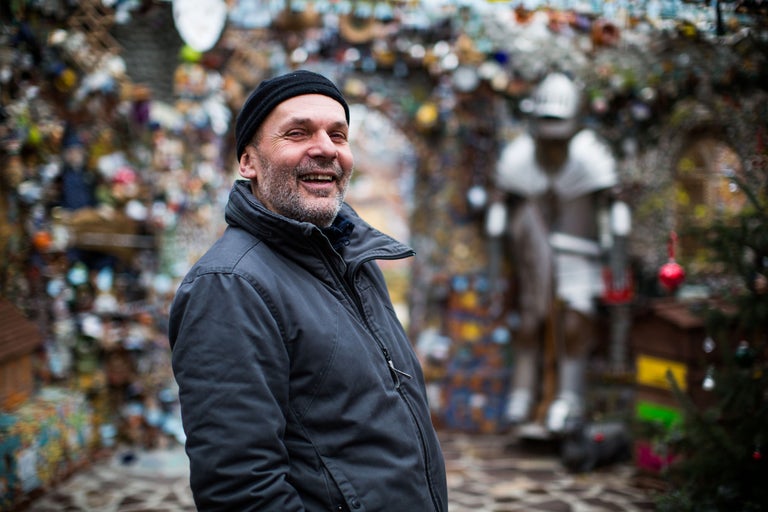 Mann mit Mütze und Jacke vor einer kunstvollen Installation im Garten