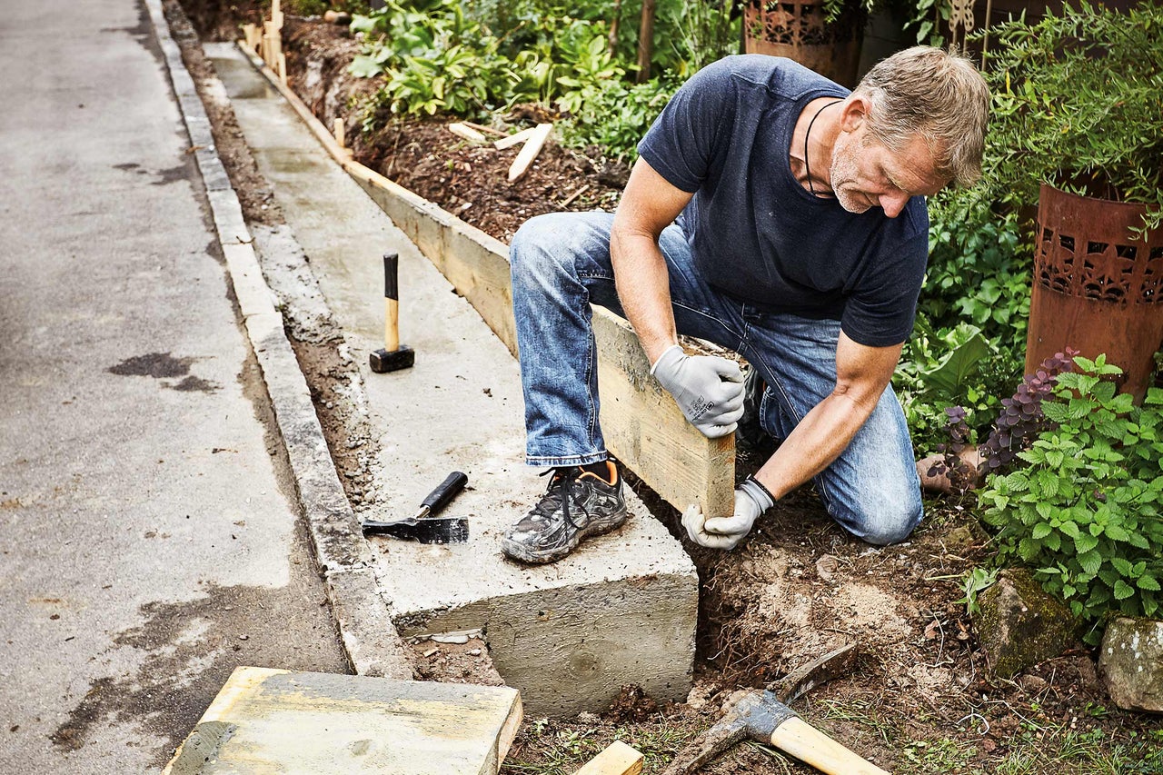 Mann arbeitet an einer Rasenkante aus Beton mit Holzschalung in einem Garten.