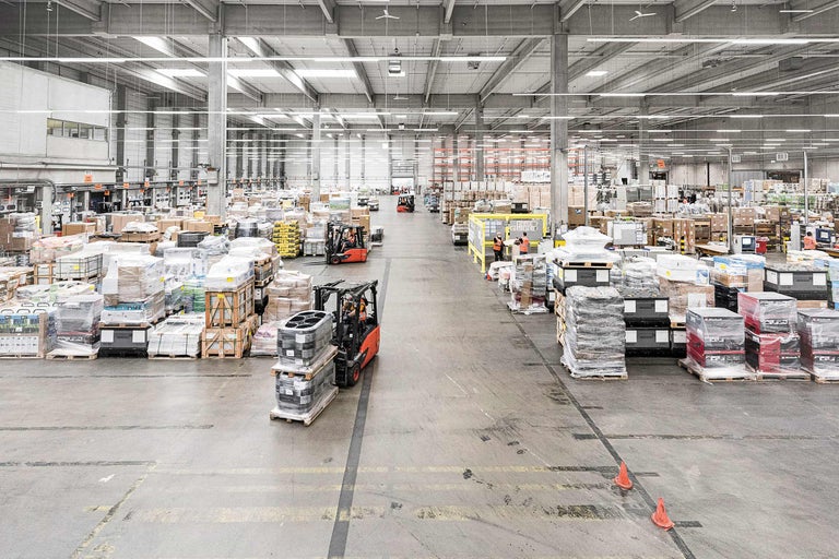 Innenansicht eines Lagers mit Gängen, gefüllt mit Paletten und einem Gabelstapler.