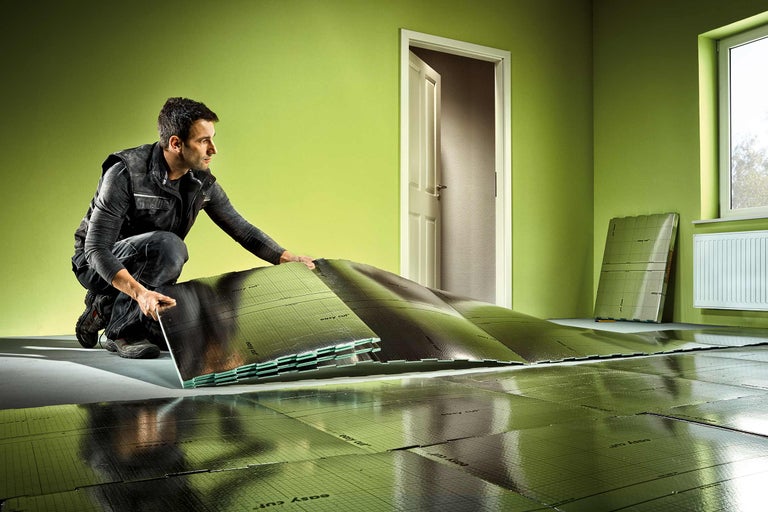 Ein Mann verlegt Dämmplatten mit Rasterdruck in einem Raum.