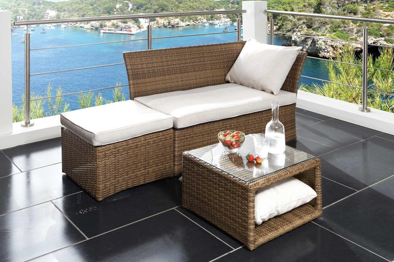 Terrasse mit Rattanmöbeln, bestehend aus Bank, Hocker und Tisch mit Glasplatte