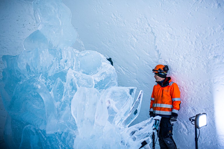 Mann mit Schutzhelm und Warnjacke in einer Eishöhle