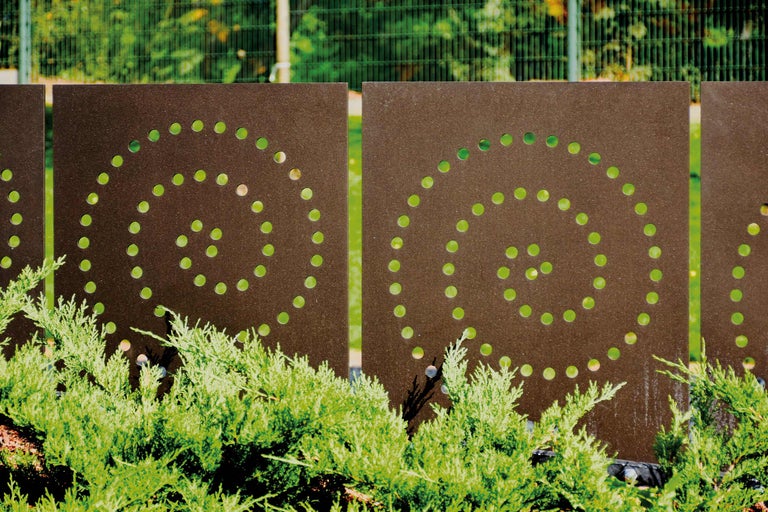 Dekorative Metallzaunelemente mit kreisförmigem Lochmuster und grüner Bepflanzung