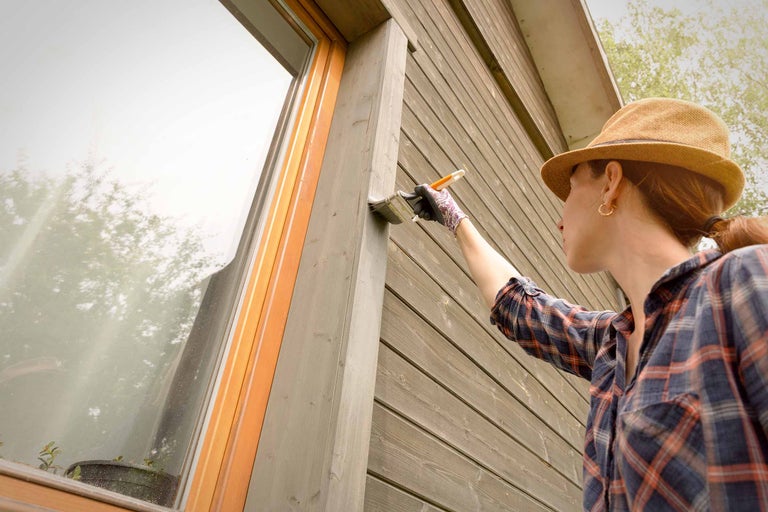 Frau streicht Holzfassade mit Pinsel