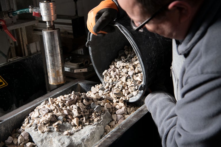 Eine Person schüttet Kies aus einem Eimer in einen Behälter.