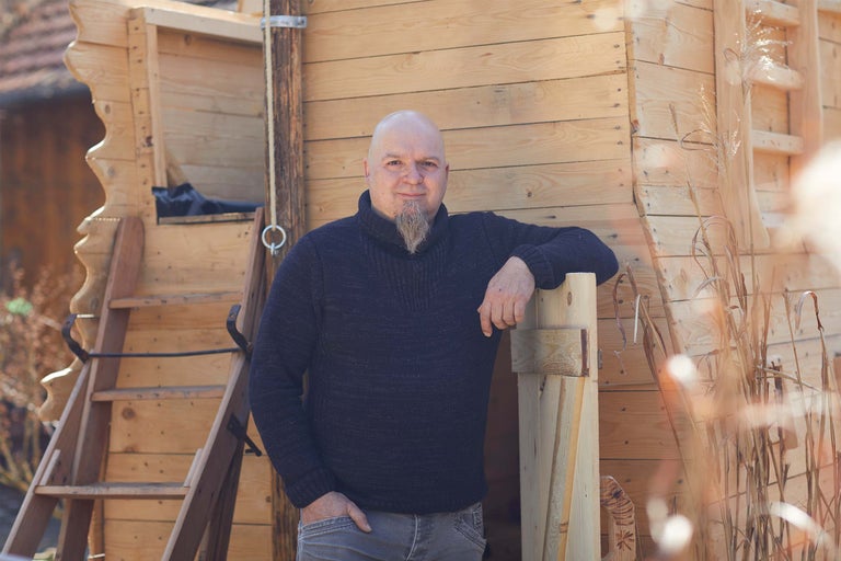 Mann steht vor einem Holzhaus mit Leiter.