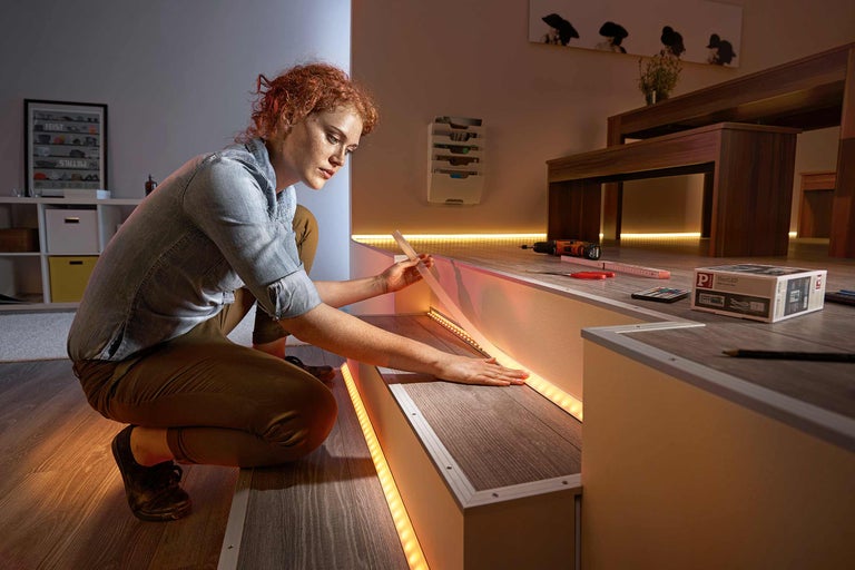 Frau befestigt LED-Streifen an einer Treppe zur dekorativen Beleuchtung.