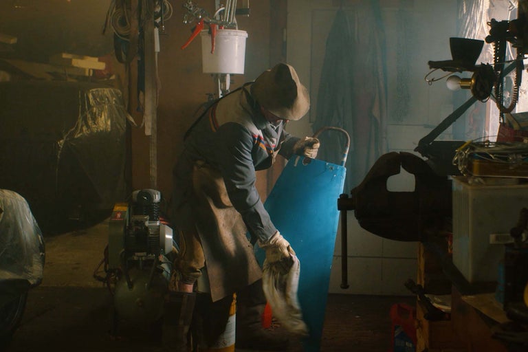 Werkstatt-Szene mit einer Person, die eine blaue Metallplatte reinigt, umgeben von Werkzeugen und Geräten.