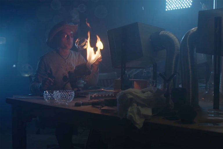 Eine Person arbeitet an einer Werkbank mit Glas und Feuer.