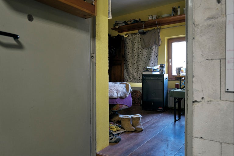 Blick durch eine Tür in ein Zimmer mit Bett, Heizung und persönlichen Gegenständen