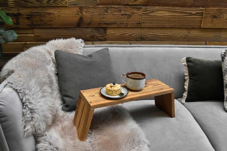 Szene mit Tablett, Tasse, Kuchen und Kissen auf Sofa vor Holzwand